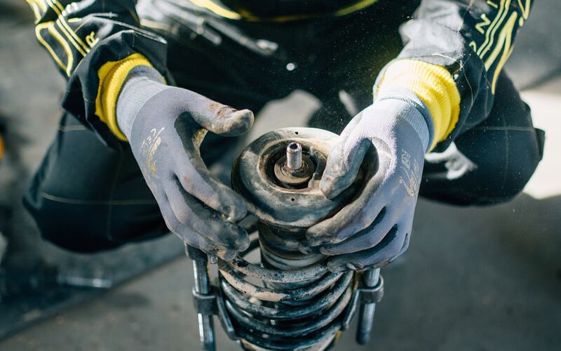 Mechanic in gloves holding a strut and coil spring assembly removed from a vehicle