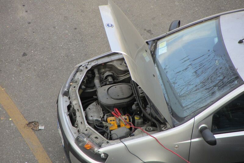 Small car with the hood open and a charger clipped to its weak battery (similar vehicle)