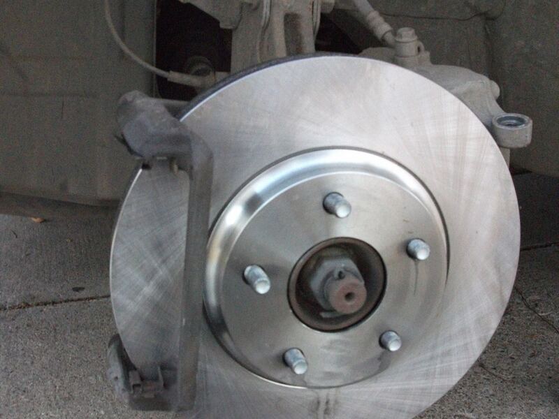 Car front brake with the wheel removed, showing a new rotor and caliper bracket