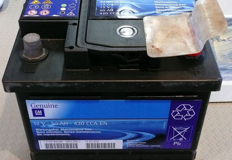 Old 12-volt GM car battery removed from a vehicle, with a dirty, peeling top cover