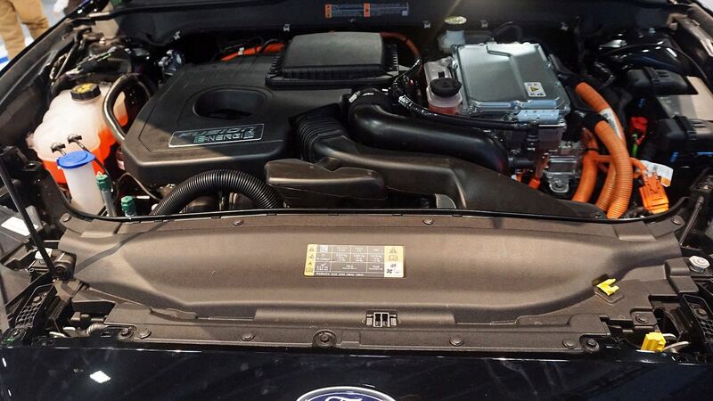 Open engine bay of a Ford Fusion Energi hybrid with the coolant reservoir and inverter visible
