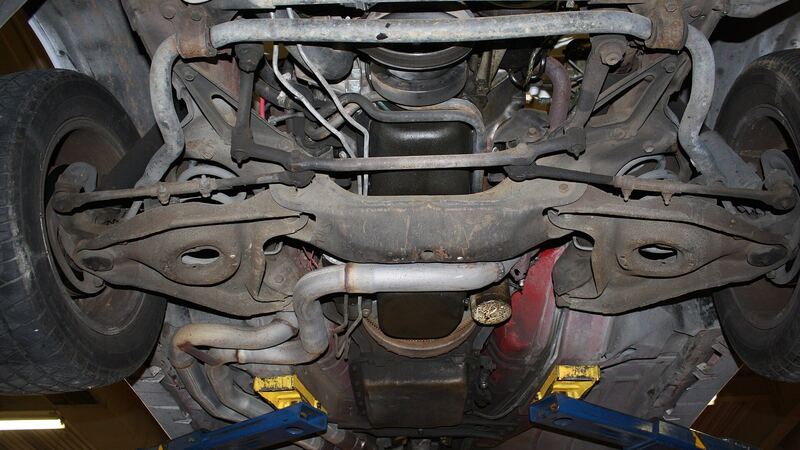 Underside of a car on a lift showing front suspension crossmember and control arms, similar vehicle