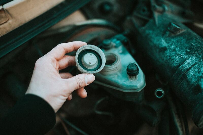 Hand opening a fluid reservoir cap in a car engine bay during a fluid check (similar vehicle)