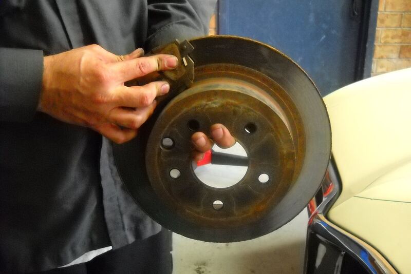 Mechanic holding a worn brake pad against a removed brake rotor (similar vehicle)