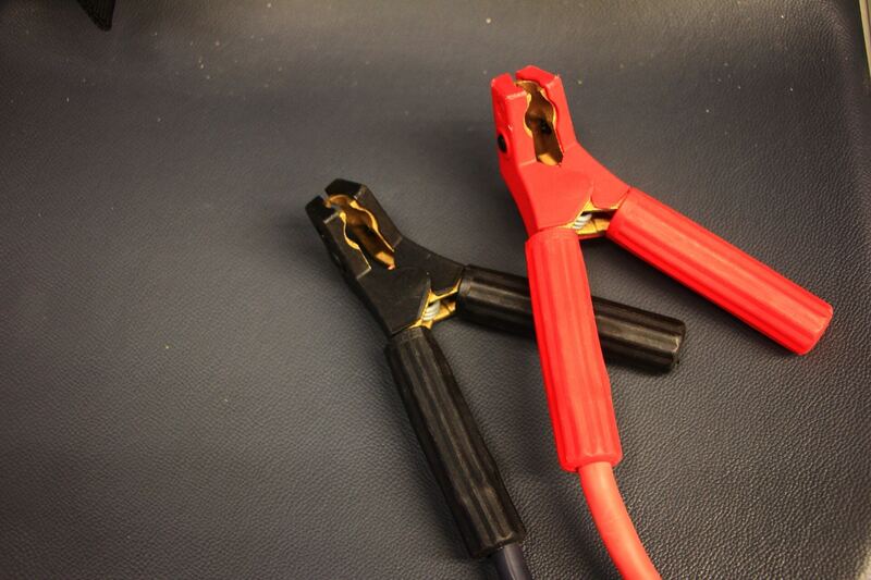 Red and black jumper cable clamps used to jump-start a car with a dead battery