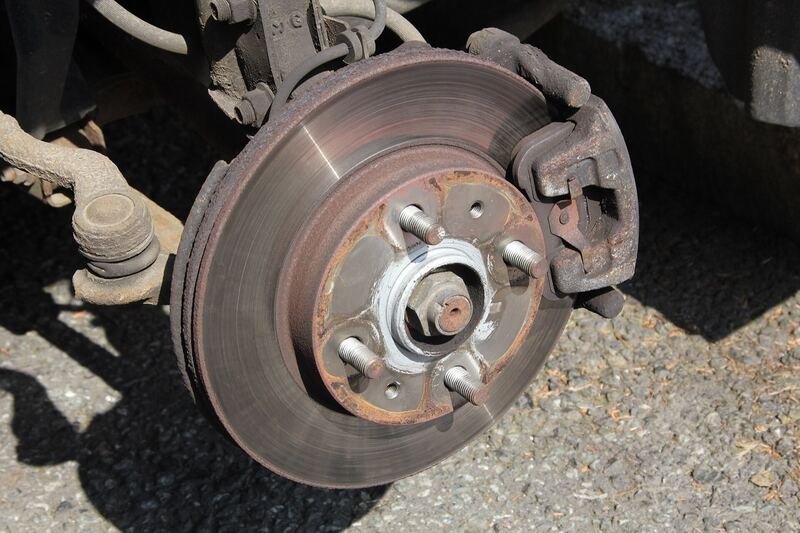 Front disc brake, caliper and rotor of a car with the wheel removed, parked on gravel (similar vehicle)