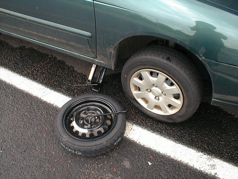 Car on a jack with a flat tire removed and the spare being fitted