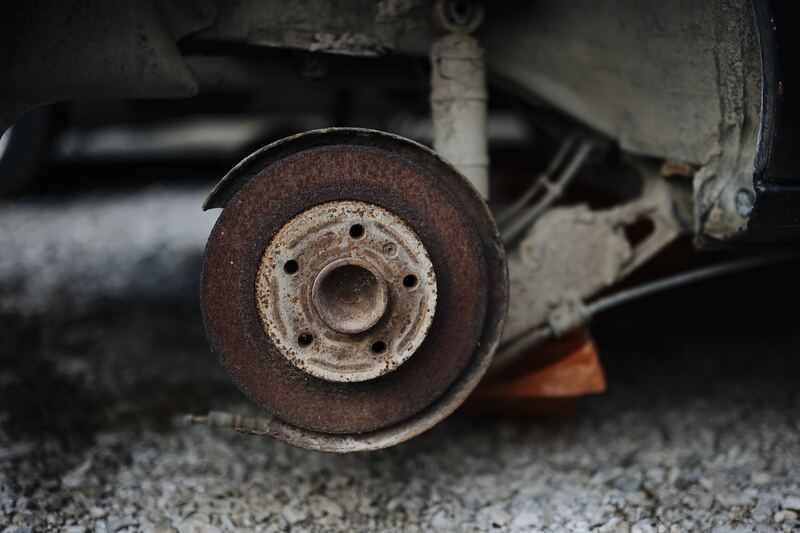 Rusty brake rotor on a car with the wheel removed, parked on gravel