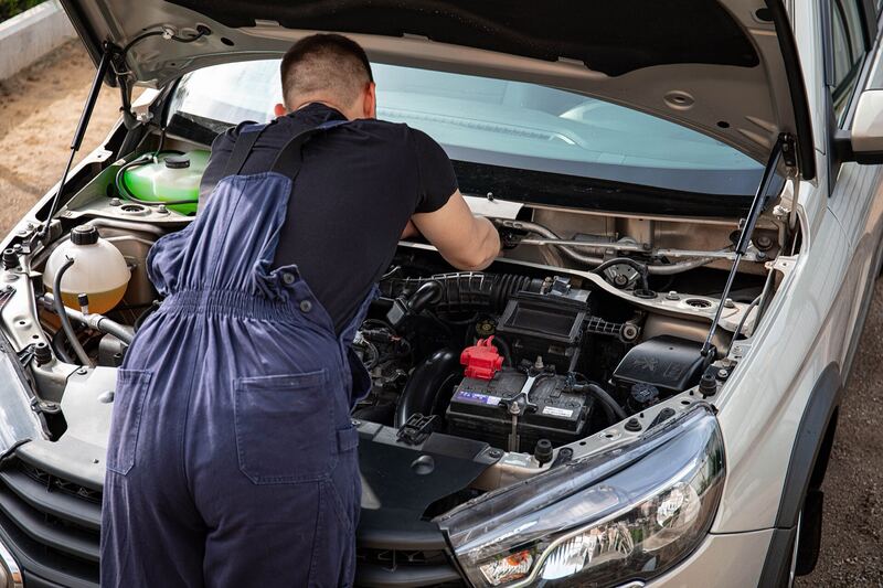 Mechanic checking the battery under the open hood of a silver car (similar vehicle)