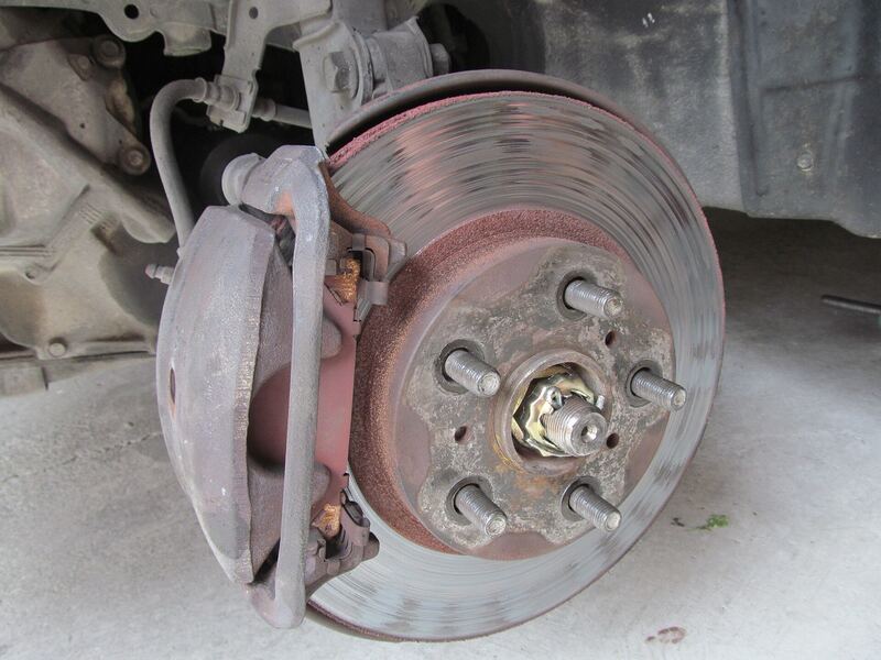 Worn front brake rotor and caliper on a car with the wheel off (similar vehicle)
