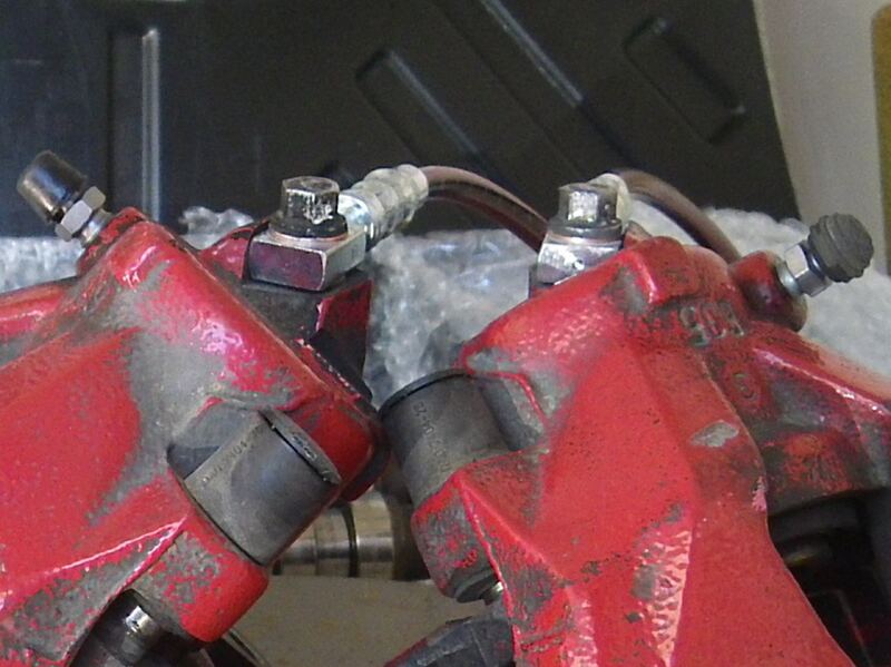 Two worn red brake calipers with brake hose fittings, removed from a vehicle (similar vehicle)