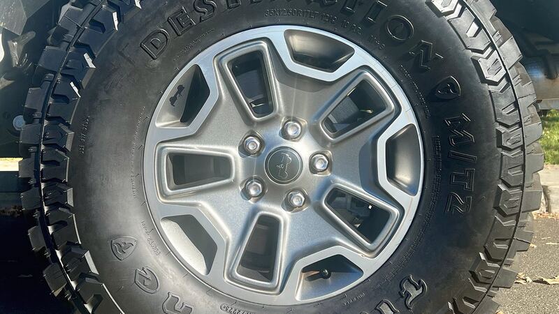 Close-up of a Jeep wheel with a mud-terrain tire and the suspension behind it, similar to a Gladiator