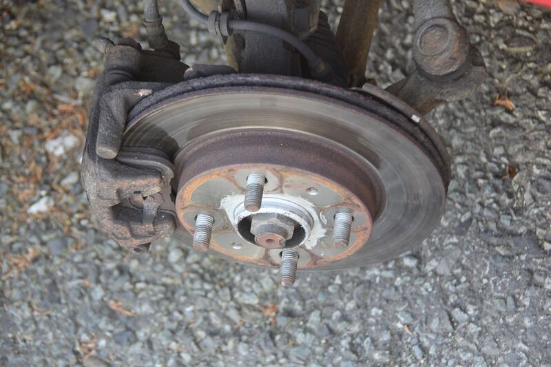 Front brake rotor and caliper on a car with the wheel removed, parked on gravel (similar vehicle)