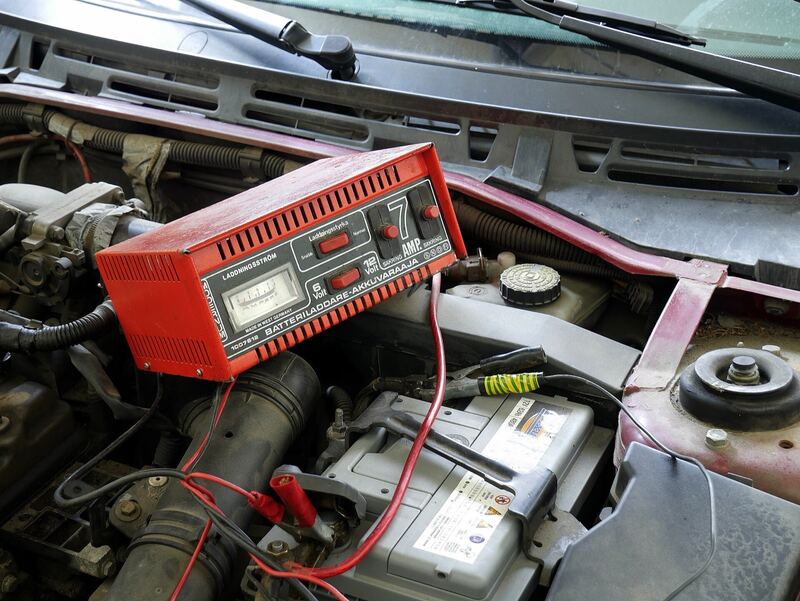 Charger clamped to a car battery under an open hood (similar vehicle, not a Sportage)