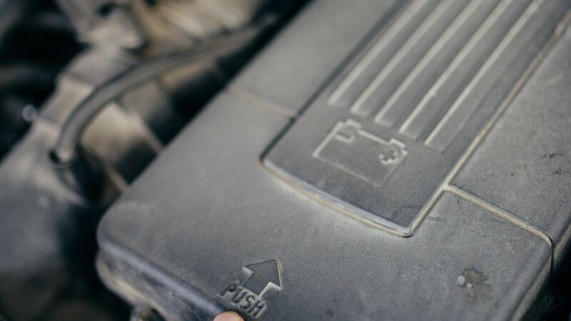 Hand pointing at the battery cover in an open car engine bay