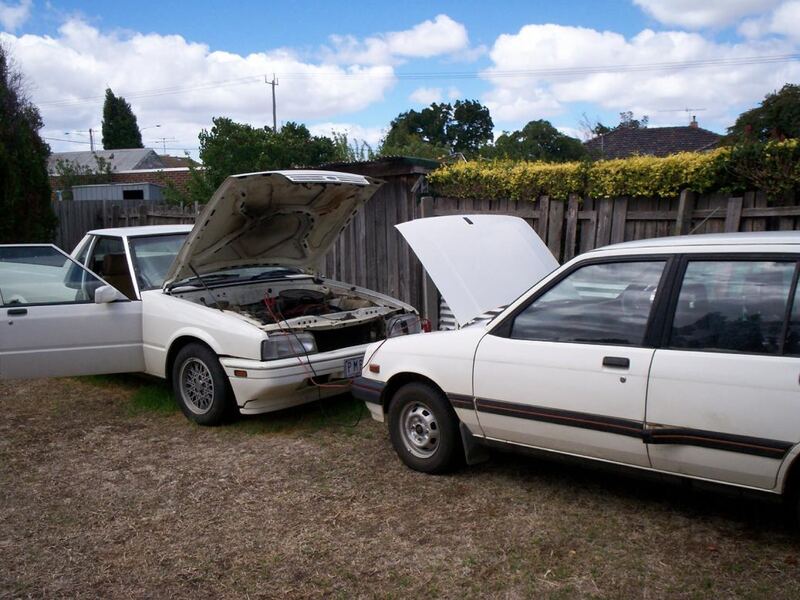 Two cars with hoods up connected by jumper cables for a jump start (similar vehicles)