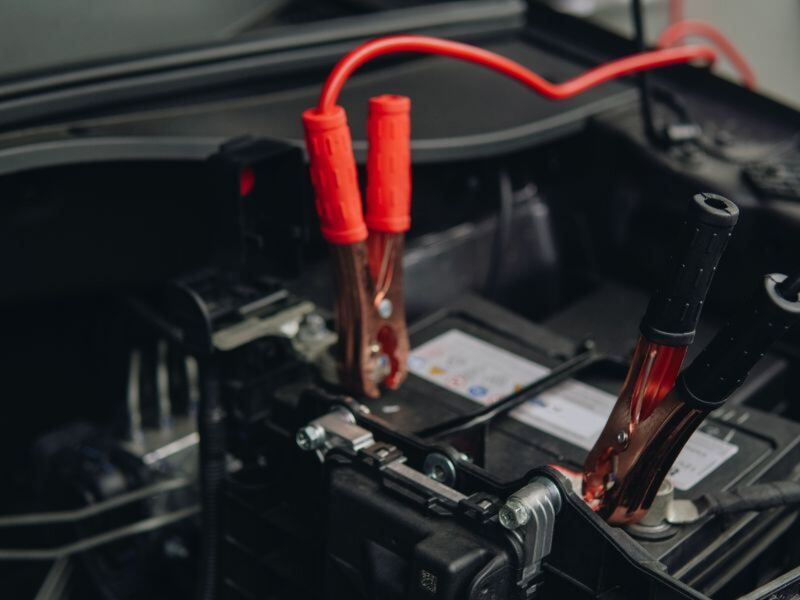 Jumper cable clamps connected to a car battery under the hood (similar vehicle)