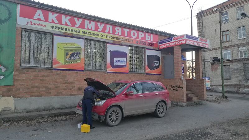 Red SUV with its hood open getting a new battery outside a battery shop (similar vehicle)