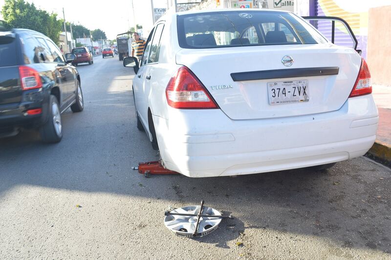 White sedan jacked up at the roadside with one wheel removed