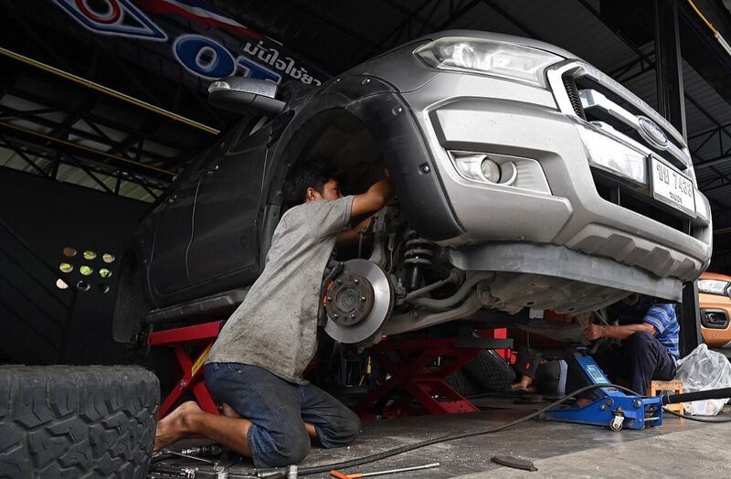 Mechanics working on a lifted pickup truck with the front wheel off and the brake rotor exposed (similar truck)